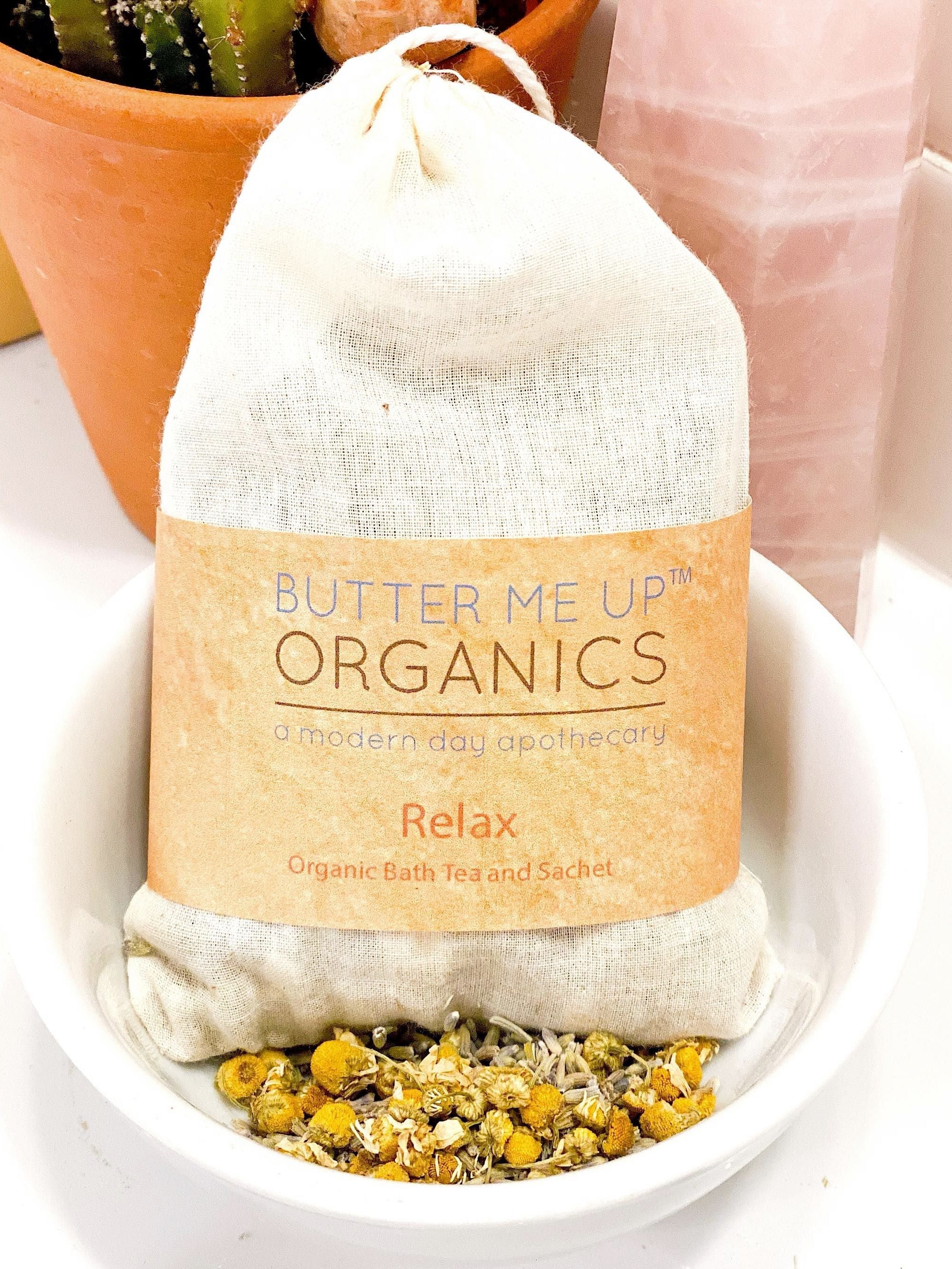 Butter Me Up Organics bath tea package with herbs in a white dish, cactus plant in the background.