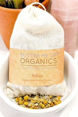 Butter Me Up Organics bath tea package with herbs in a white dish, cactus plant in the background.