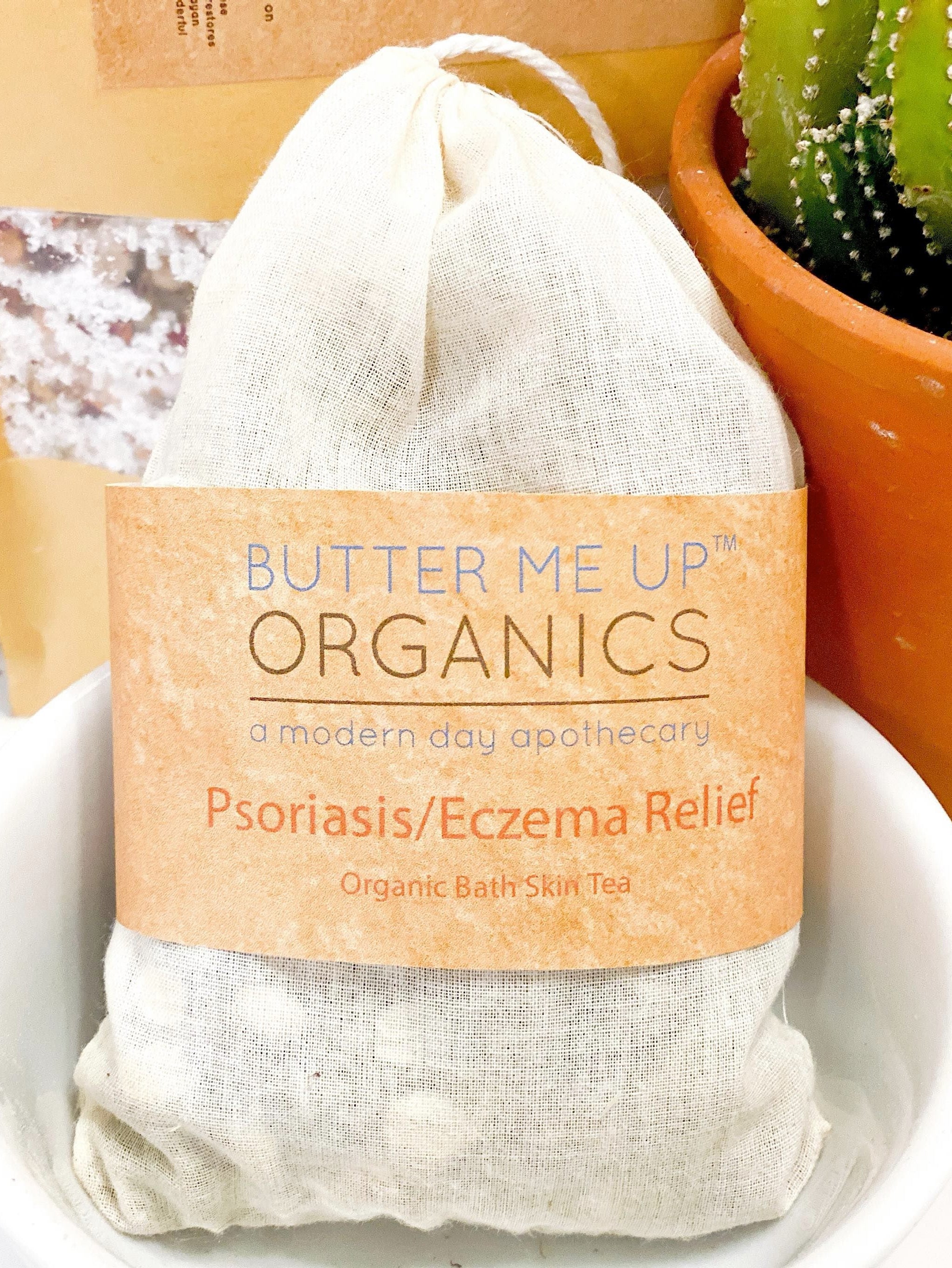 Bag of 'Butter Me Up Organics' Psoriasis/Eczema Relief bath skin tea with a cactus plant in the background.