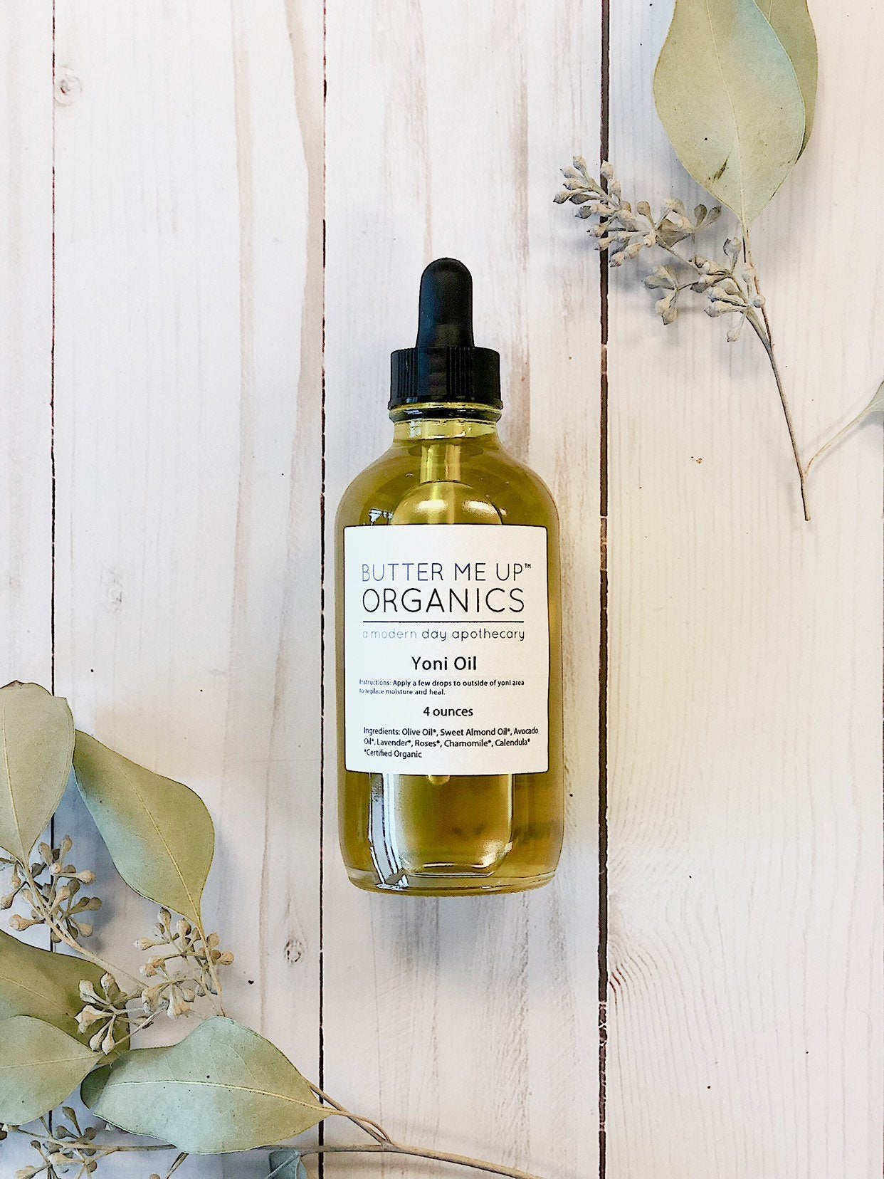 Butter Me Up Organics Yoni Oil bottle with dropper on a wooden surface with leaves.