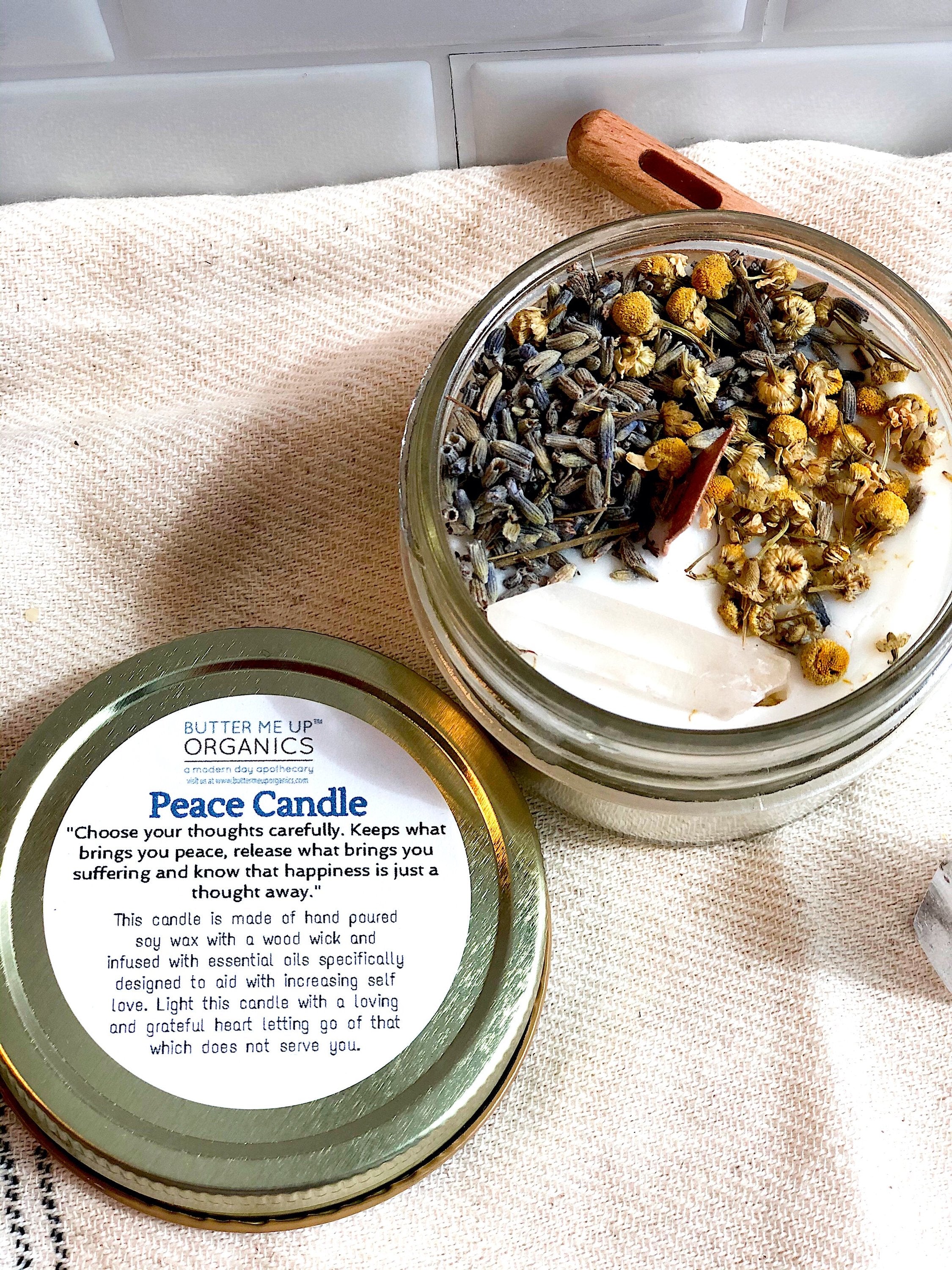 Peace Candle packaging with lid open showing lavender and wood chips on a beige cloth.