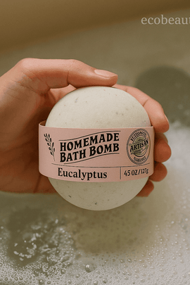 Person holding eucalyptus bath bomb above foamy bath water, showcasing natural handmade design and pastel pink label, ecobeaut.com