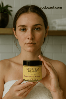 A woman wrapped in a white towel holds a jar of Butter Me Up Organics Clear Face Facial Moisturizer in front of a softly blurred bathroom background.