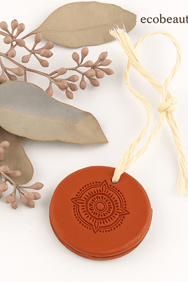 Red compact case with decorative emblem on a white background with dried leaves and branches.