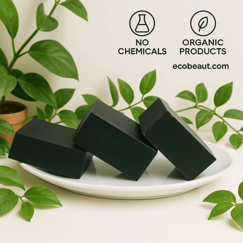 Three charcoal soap bars by ecobeaut.com arranged on a white plate surrounded by green leaves, with “NO CHEMICALS” and “ORGANIC PRODUCTS” icons and the website in the upper right corner.



