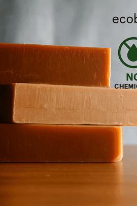 Three stacked rectangular bars of handcrafted soap in earthy tones on a wooden surface, with “NO CHEMICALS,” “ORGANIC PRODUCTS” icons and the website “ecobeaut.com” displayed in the upper right corner against a soft gray background.




