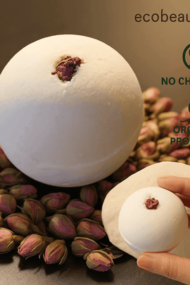 White goat's milk and honey bath bomb with dried rosebud on top, styled on a bed of pink rosebuds – organic product with no chemicals, ecobeaut.com