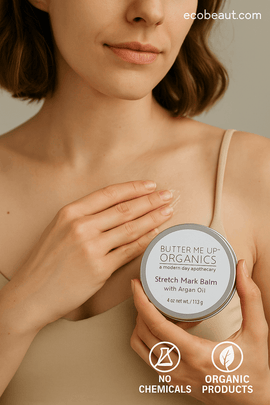 Woman applying Butter Me Up Organics Stretch Mark Balm with Argan Oil to her chest, holding an open tin with label visible, with ecobeaut.com, no chemicals, and organic products icons in the top right corner