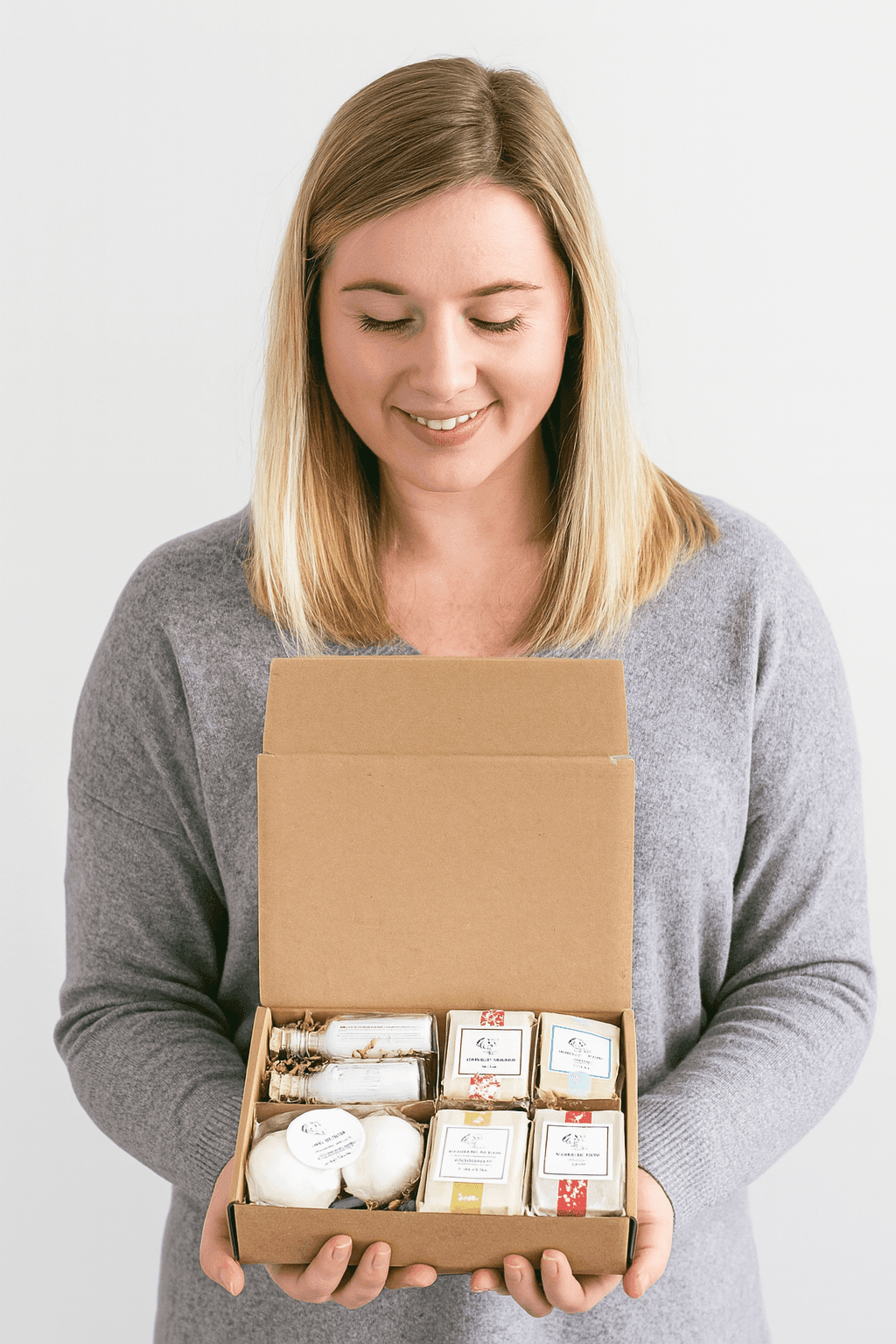 Woman holding eco-friendly gift set with natural handmade soaps, bath bombs, and organic skincare products in a kraft box – perfect sustainable gift idea, premium USA-made natural cosmetics for self-care and relaxation