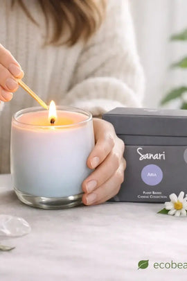 Person lighting a candle with 'Sanari' packaging in the background, surrounded by flowers and plants.
