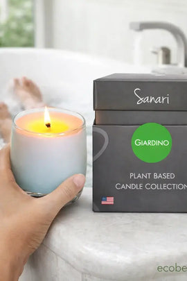 Hand holding a lit candle next to a box labeled 'Sanari Giardino' on a bathtub.