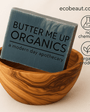  soap bar labeled 'Butter Me Up Organics' displayed in a carved wooden bowl with the text ecobeaut.com in the top right corner and icons reading 'no chemicals' and 'organic products' on a neutral background.